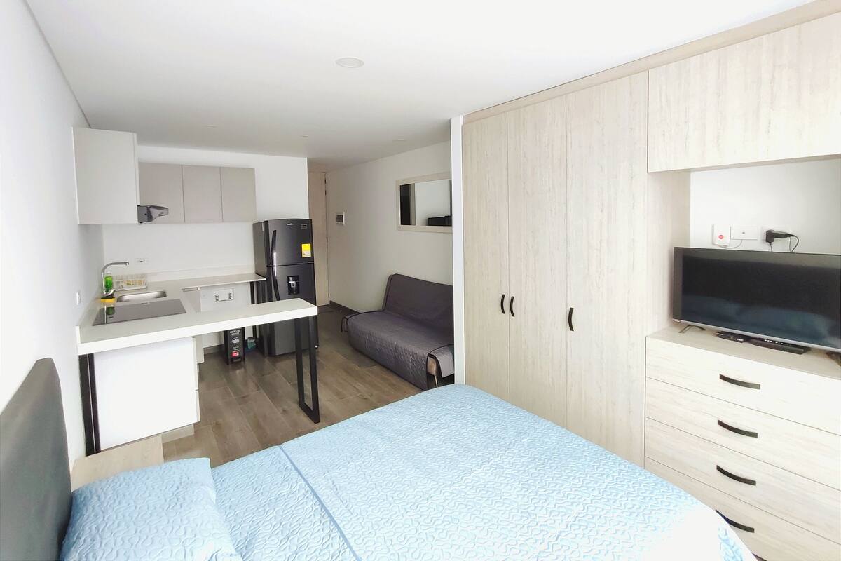 Une chambre de taille réduite comprenant un lit, un téléviseur, une kitchenette et une armoire.