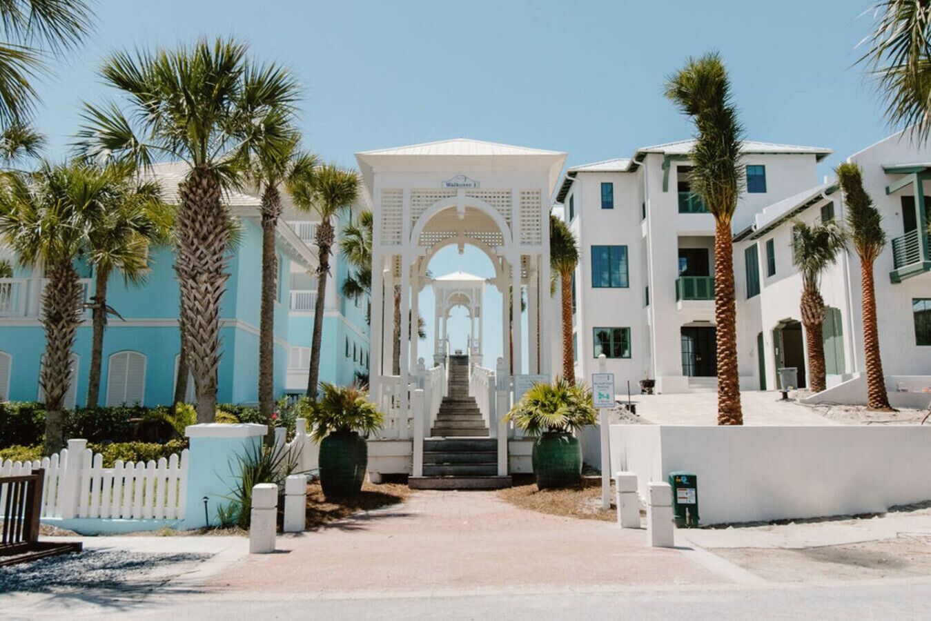 A hotel entrance with a central archway, palm trees, and a white picket fence.