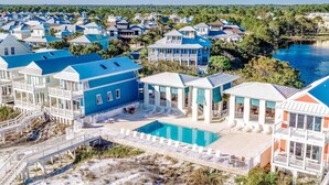 A coastal resort with multiple blue-roofed buildings, a central swimming pool, and a beach area with white railings.