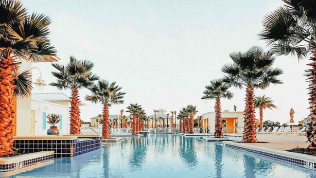 A swimming pool surrounded by palm trees and buildings with a clear sky.