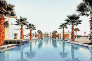Une piscine entourée de palmiers et de bâtiments, avec un ciel dégagé.
