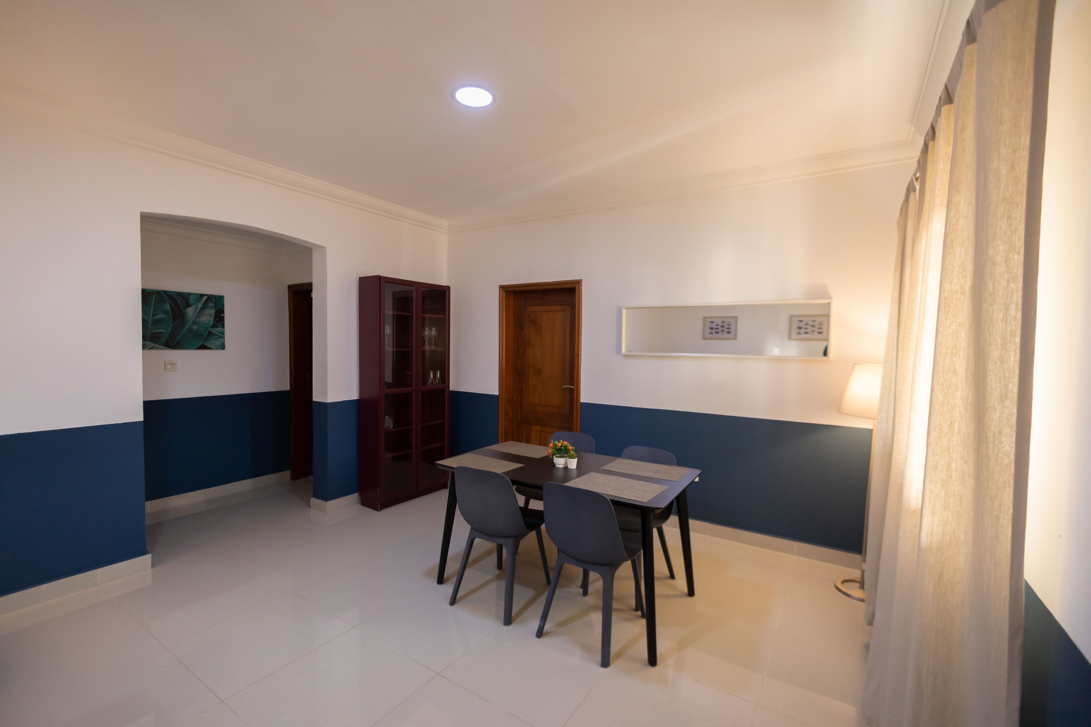 A dining area with a table and chairs, a cabinet, and a wall-mounted control panel.