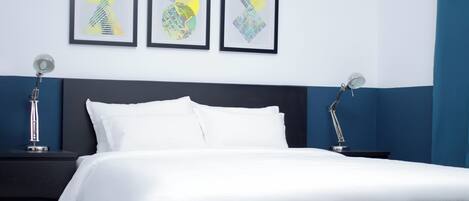 A modern bedroom with a black headboard, white bedding, and three framed abstract artworks on the wall.