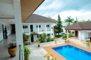 A pool area with a tiled deck, surrounded by potted plants and a building with a tiled roof. - BRAGHA APARTMENTS (Sekondi-Takoradi)