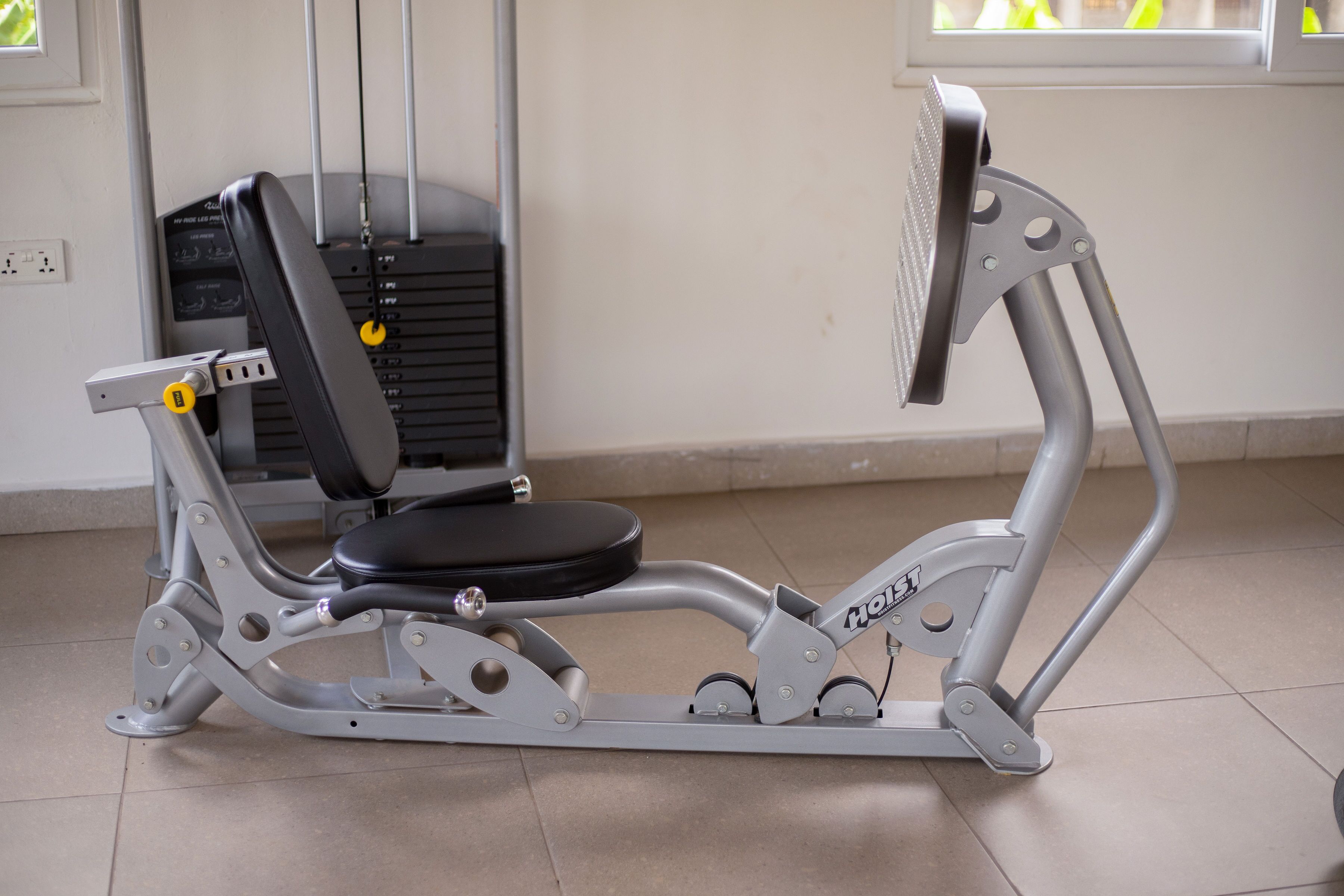 A stationary exercise bike with a control panel, located in a room with a tiled floor and a window with blinds.