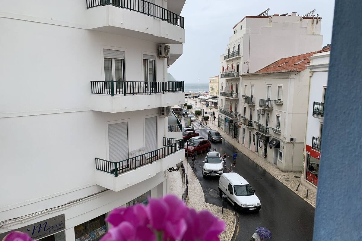 A narrow street lined with multi-story buildings, some with balconies, and parked cars.
