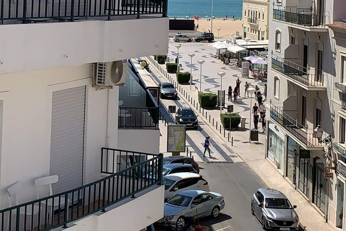 A multi-story building with balconies overlooking a street and a beach.