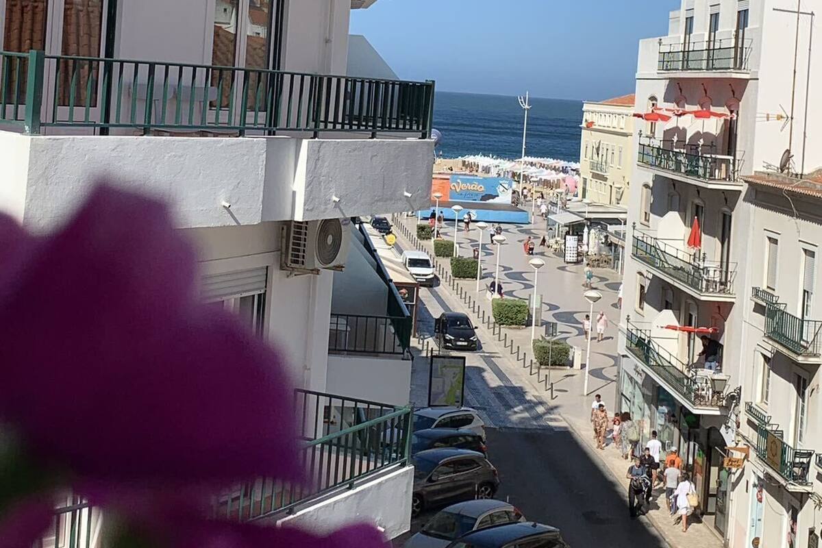 A coastal street with buildings, parked cars, and a clear view of the sea.