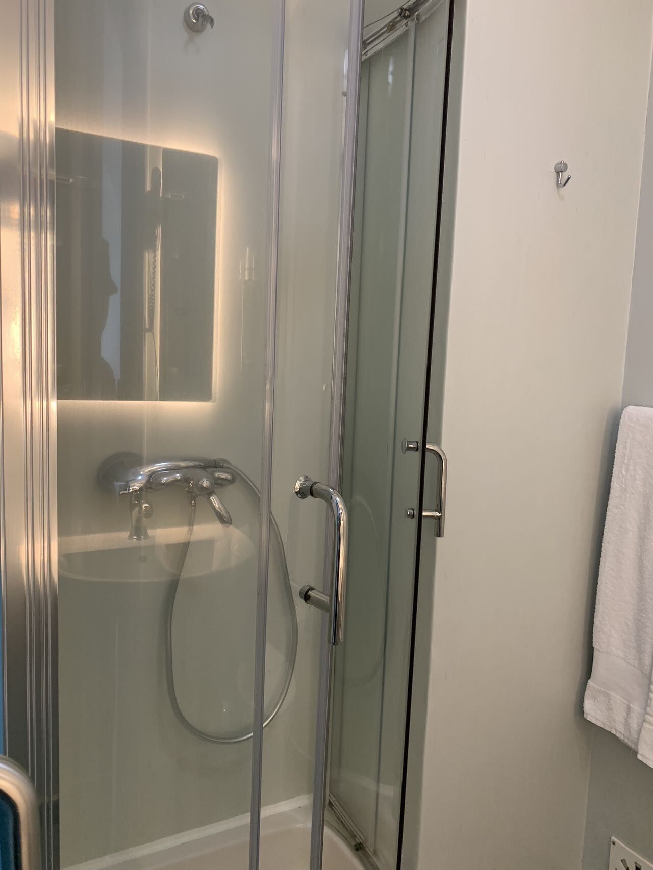Ducha envuelta en vidrio con cabezal de ducha de mano y grifo empotrado.
