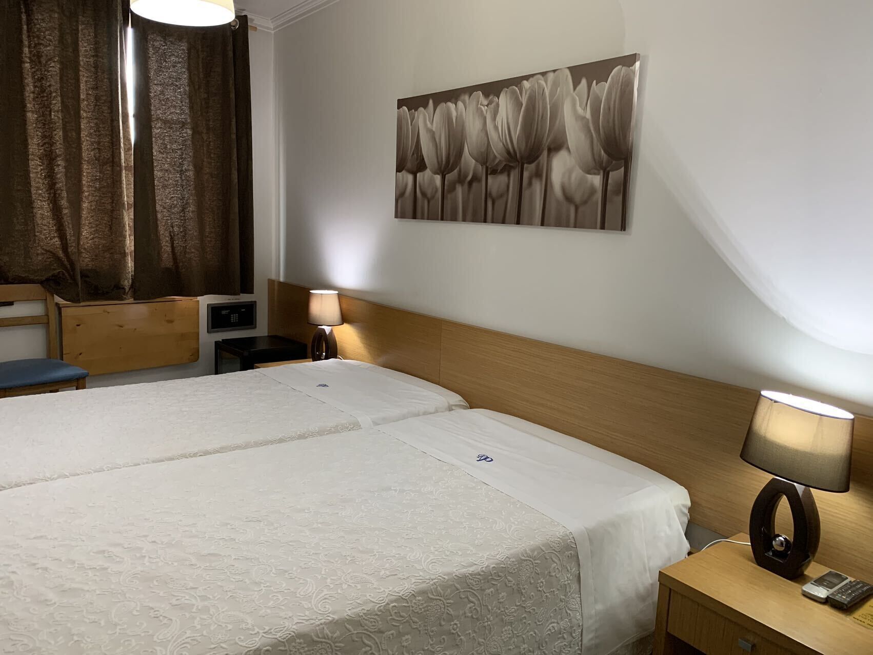 Habitación de hotel con una cama grande, dos mesitas de noche, un escritorio, una silla, una lámpara y un cuadro en la pared.