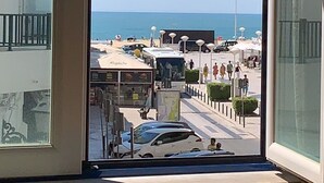 A view from a window overlooking a beachside promenade with buildings, a bus, and a clear sky. - WEAA Hotel (Nazaré)