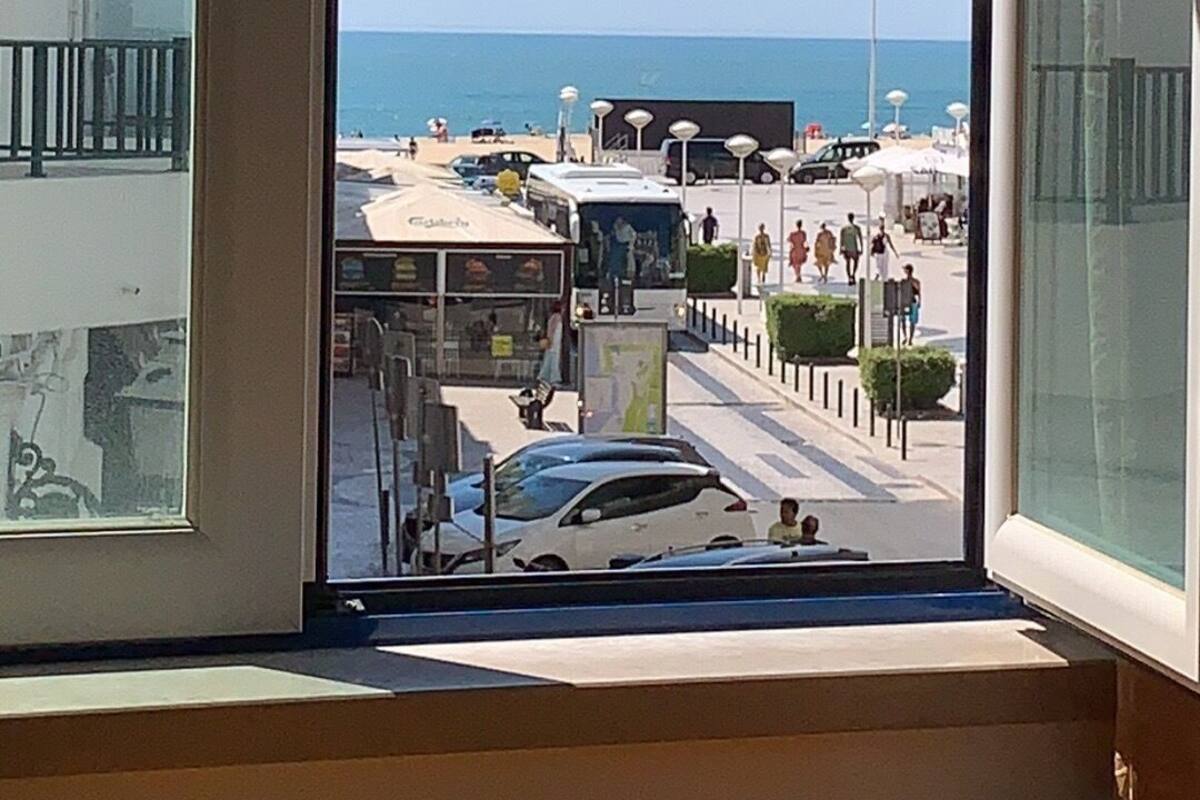 A view from a window overlooking a beachside promenade with buildings, a bus, and a clear sky.