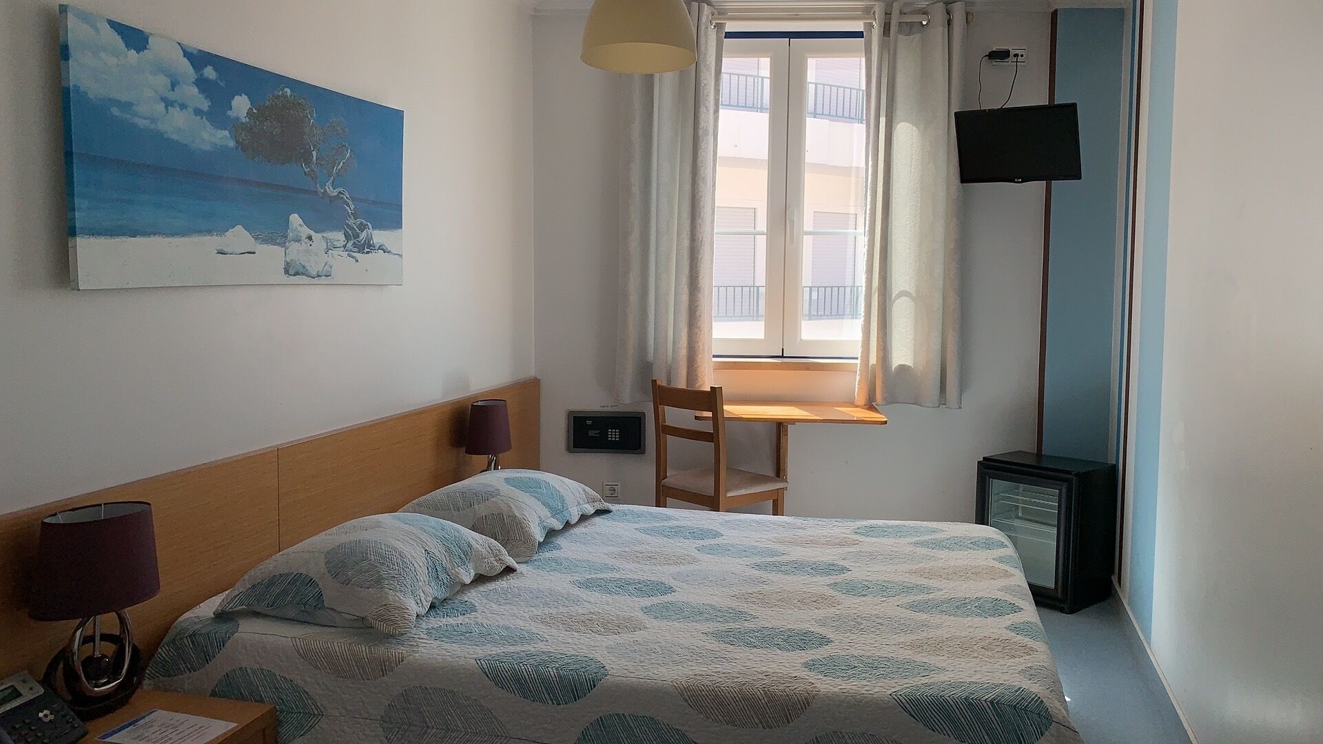 Ein Schlafzimmer mit Bett, Schreibtisch, Stuhl, Fernseher und einem Bild an der Wand.