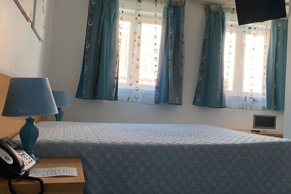 A bedroom with a bed, two bedside lamps, a telephone, a small table, and a TV.
