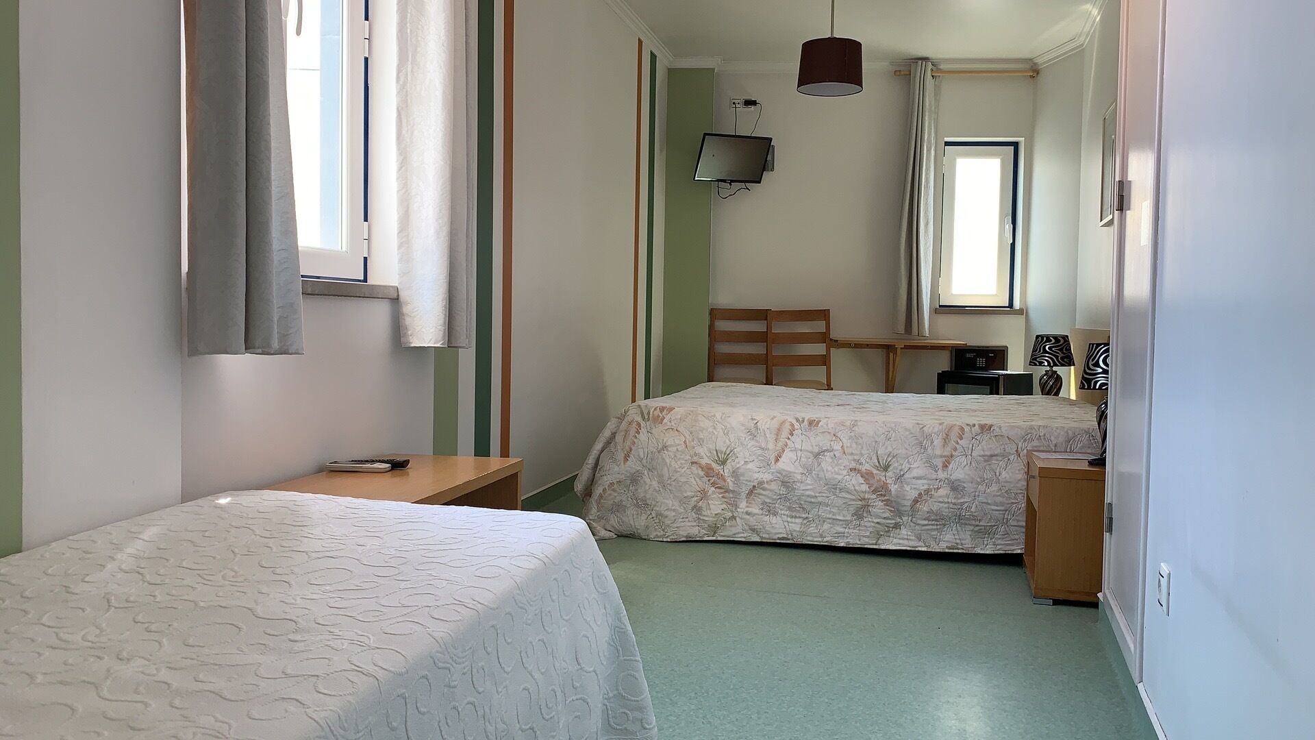 Habitació petita i neta amb dues lliteres, un escriptori, una cadira, un televisor i una finestra.