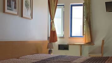 A bedroom with a large bed, a window with curtains, a ceiling light, and framed pictures on the wall.