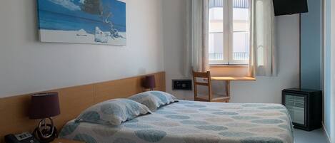A hotel room with a bed, a desk, a chair, a TV, and a painting on the wall.