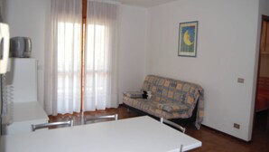 A living room with a sofa, a television on a stand, and a painting on the wall. - Welcoming Apartment With Balcony Near the Beach (San Michele al Tagliamento)