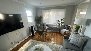 Una sala de estar con televisor de pantalla plana, sofá gris, mesa de centro blanca y una alfombra mullida.