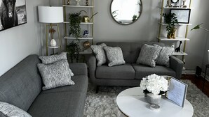 Una sala moderna con un sofá gris, almohadones estampados, una mesa de centro blanca y una alfombra mullida.