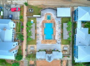 An aerial view of a residential area with a central swimming pool, surrounded by wooden decks and lounge areas.