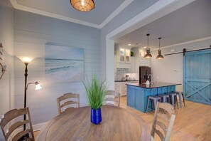A dining area with a round wooden table, chairs, a blue vase with green plants, and a wall-mounted lamp. - Watercolor Cottage (Carlton Landing)