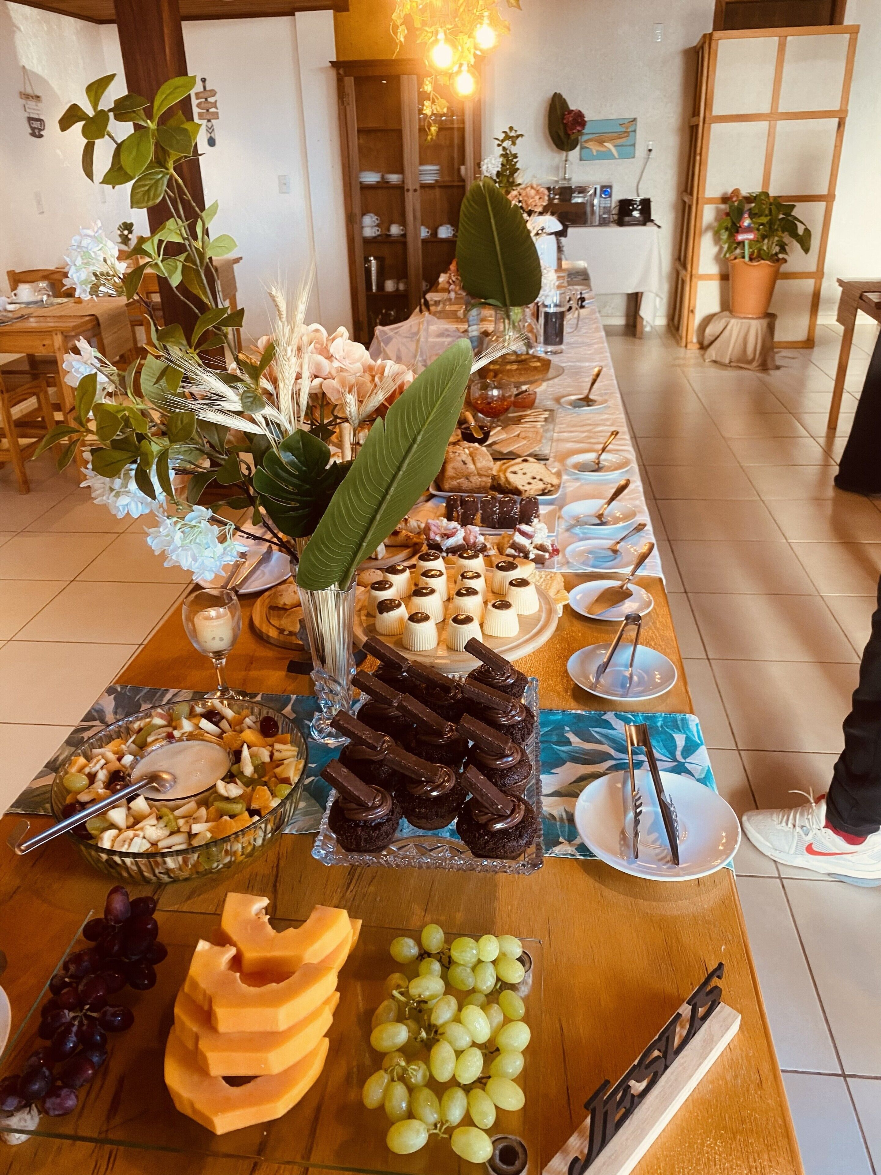 Una mesa de buffet con distintos alimentos, un florero con flores y una mesa de madera.