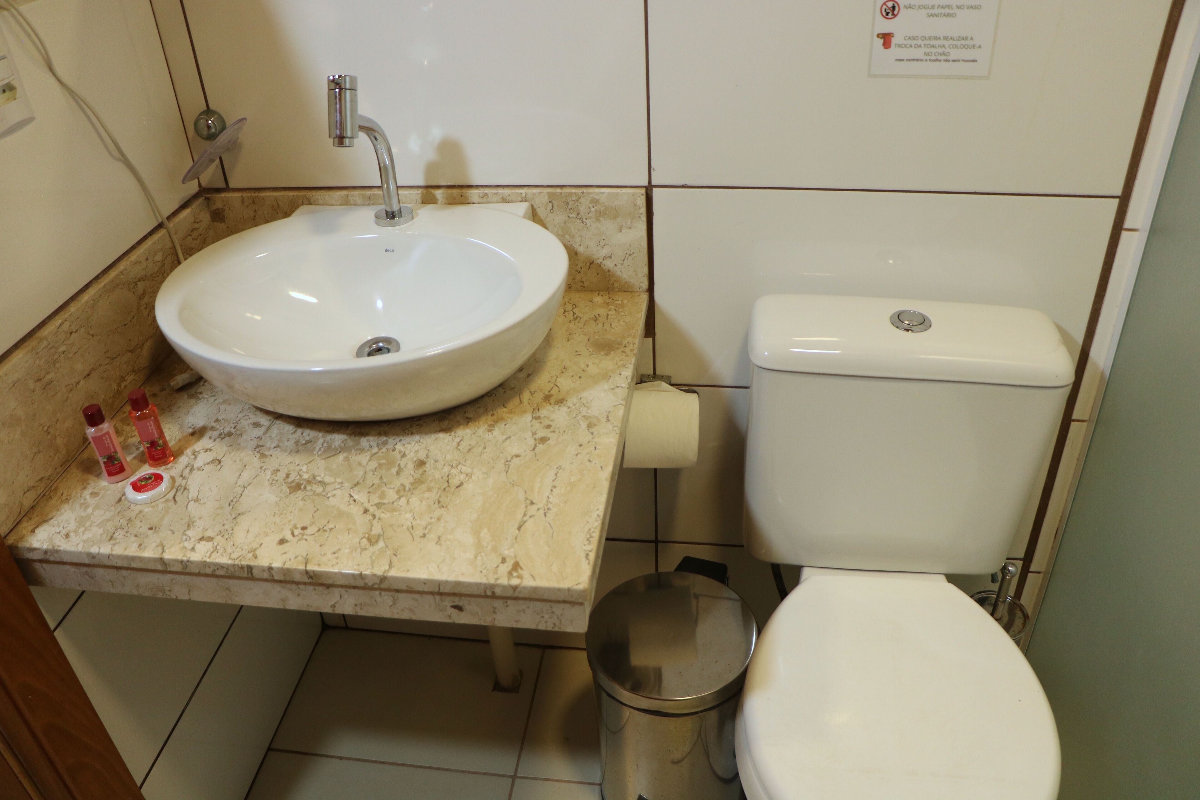 A bathroom with a sink, toilet, and trash can.