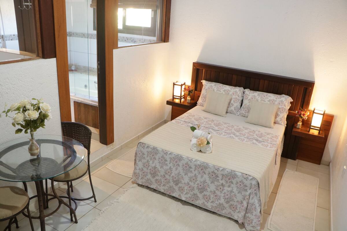 A neatly arranged bedroom with a bed, bedside tables, a small table with chairs, and a window.