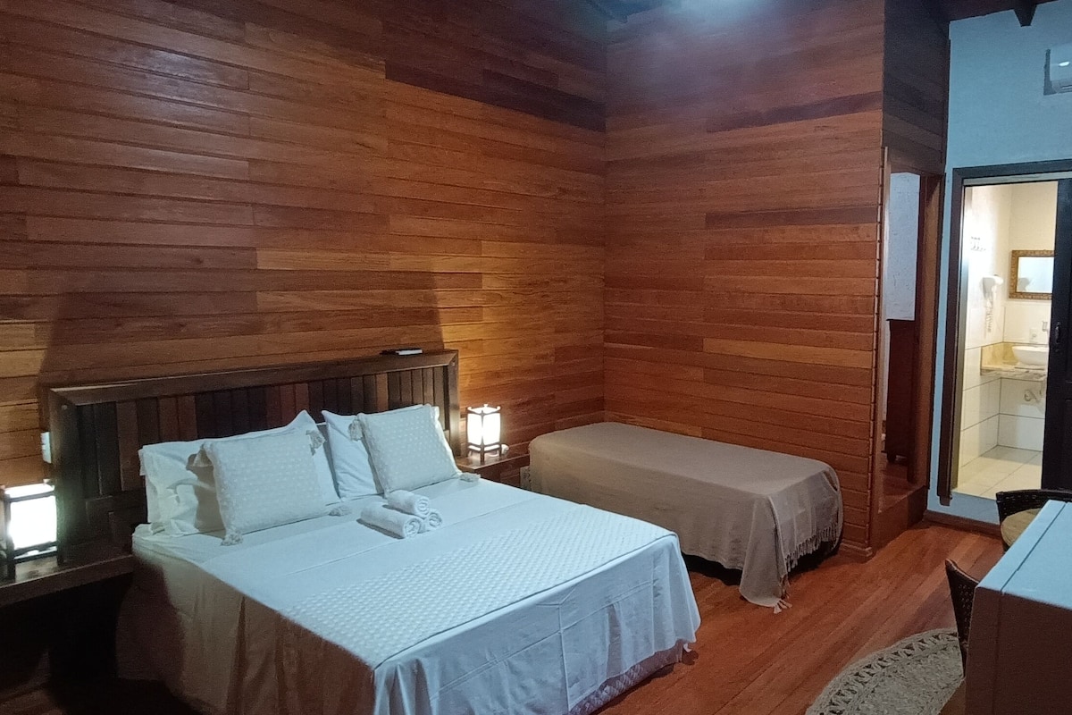 A wooden-paneled room with a bed, a smaller bed, a table, and a chair.