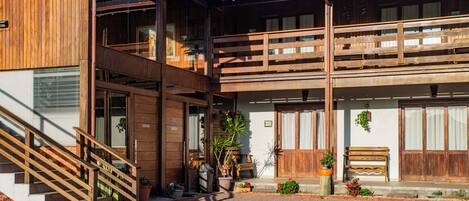 A two-story wooden building with a balcony, a staircase, and potted plants.