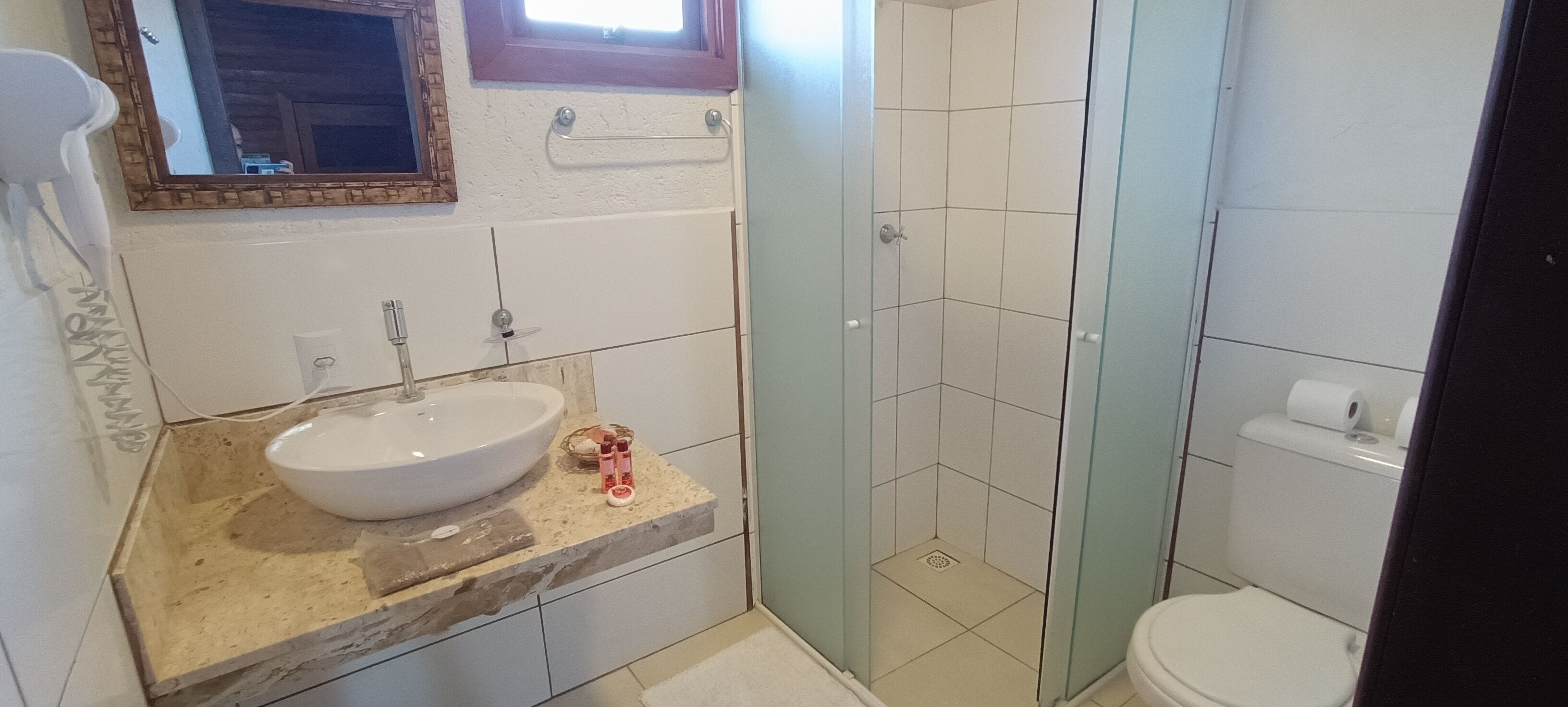 Casa de banho com lavatório branco, cabine de duche em vidro e sanita.