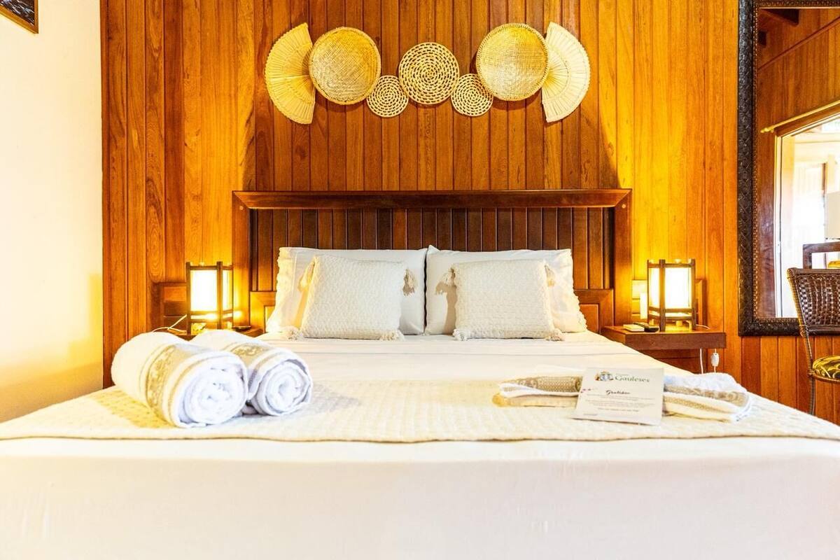 A hotel room with a wooden wall, a large bed with white bedding, two bedside lamps, and a wall-mounted decorative item.