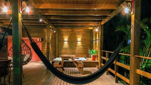 Une terrasse en bois avec un hamac, une table et des chaises, entourée de rampes en bois et de plantes en pot.