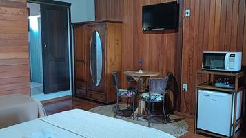 Una habitación compacta con un armario de madera, una pequeña mesa con sillas, un televisor, un microondas y un refrigerador.