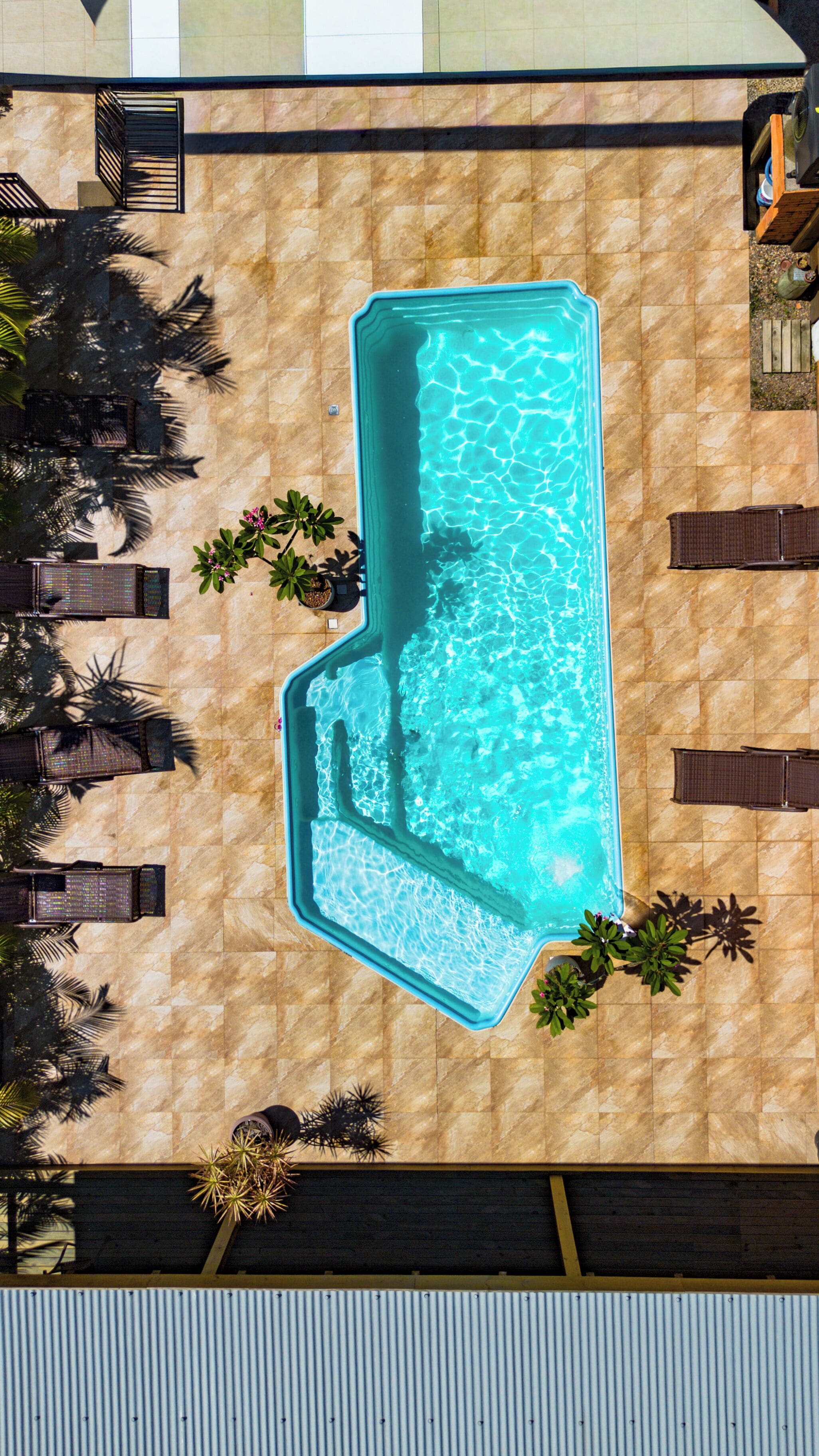 Vista aérea de una piscina rodeada de sillas de descanso y plantas en macetas.