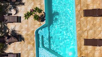 Vista aérea de una piscina rodeada de sillas de descanso y plantas en macetas.