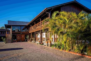 Un bâtiment traditionnel en bois, doté d’un patio couvert, de plantes en pot et d’une allée gravillonnée.