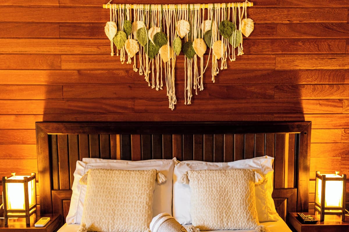 A neatly made bed with white linens, a decorative macrame hanging, and two bedside lamps.