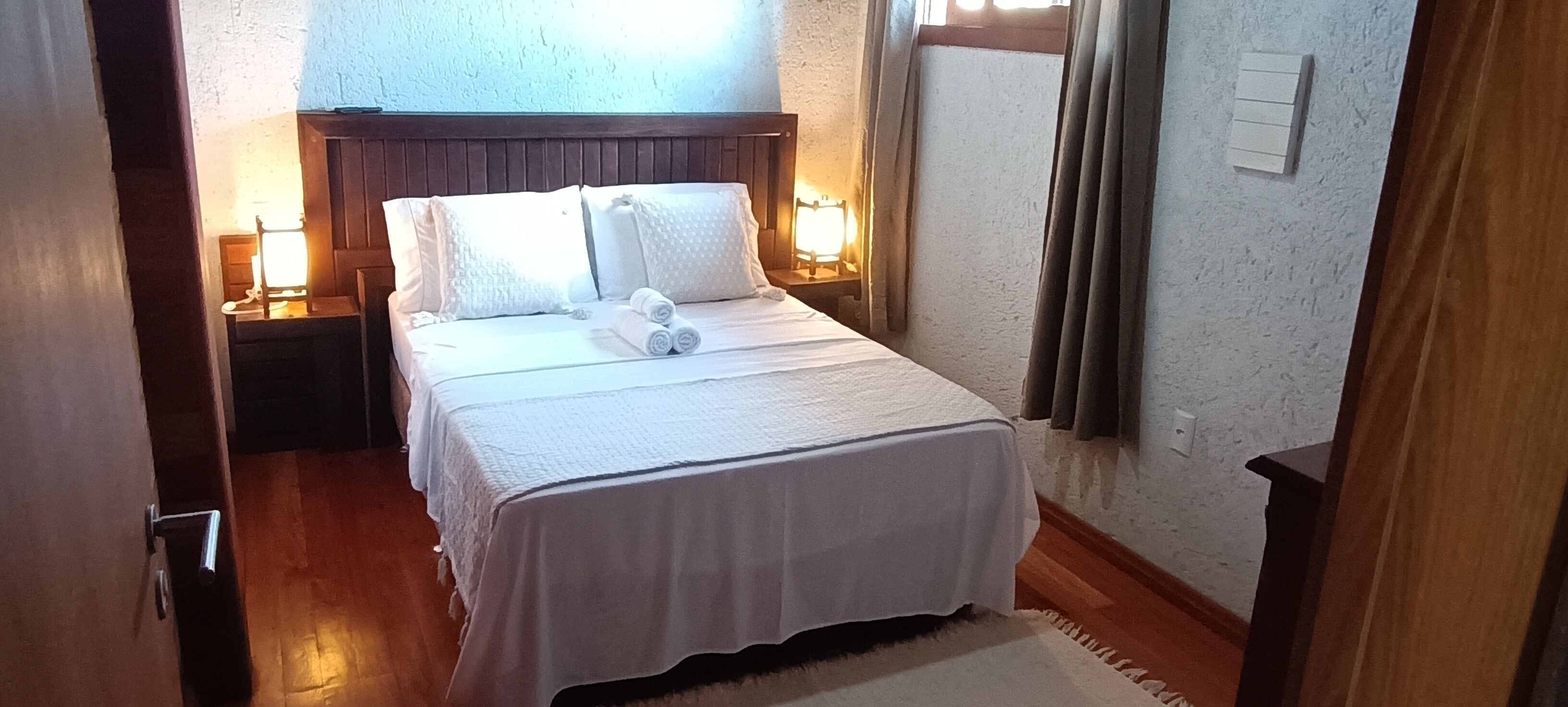 A neatly made bed with white linens and pillows, a wooden headboard, and bedside lamps.