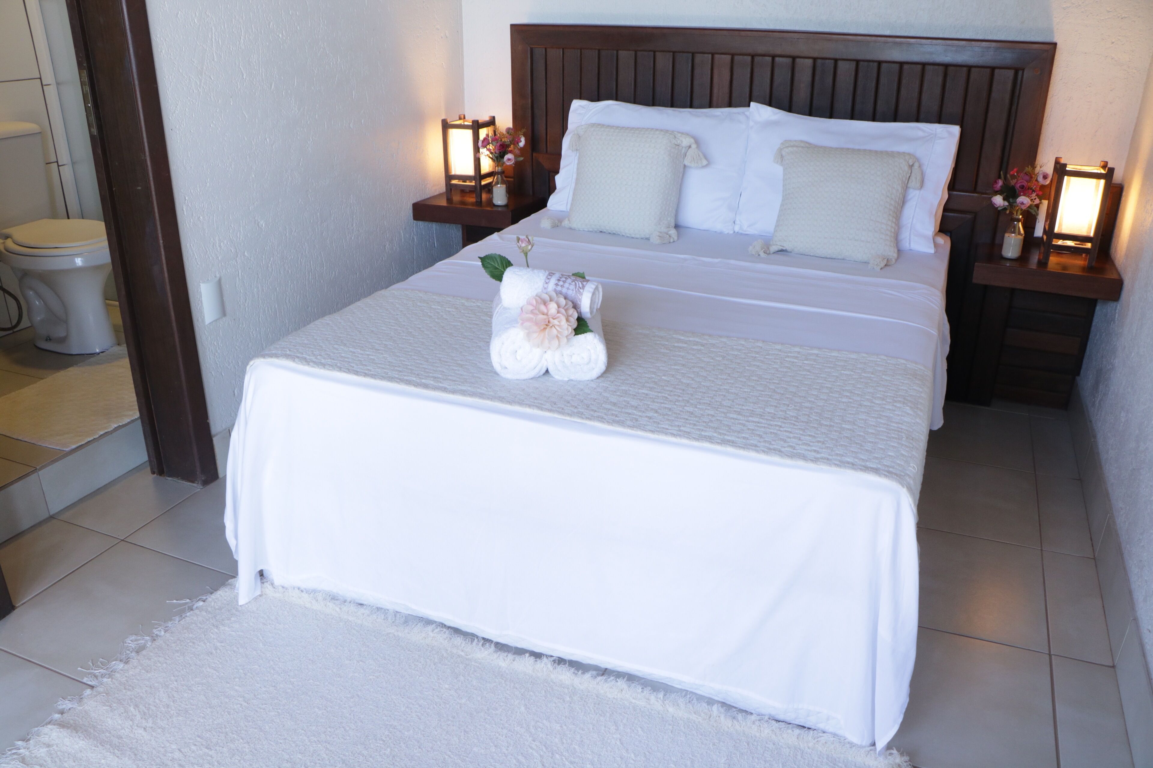 A neatly made bed with white linens, a floral arrangement on the bed, and two bedside tables with lamps.