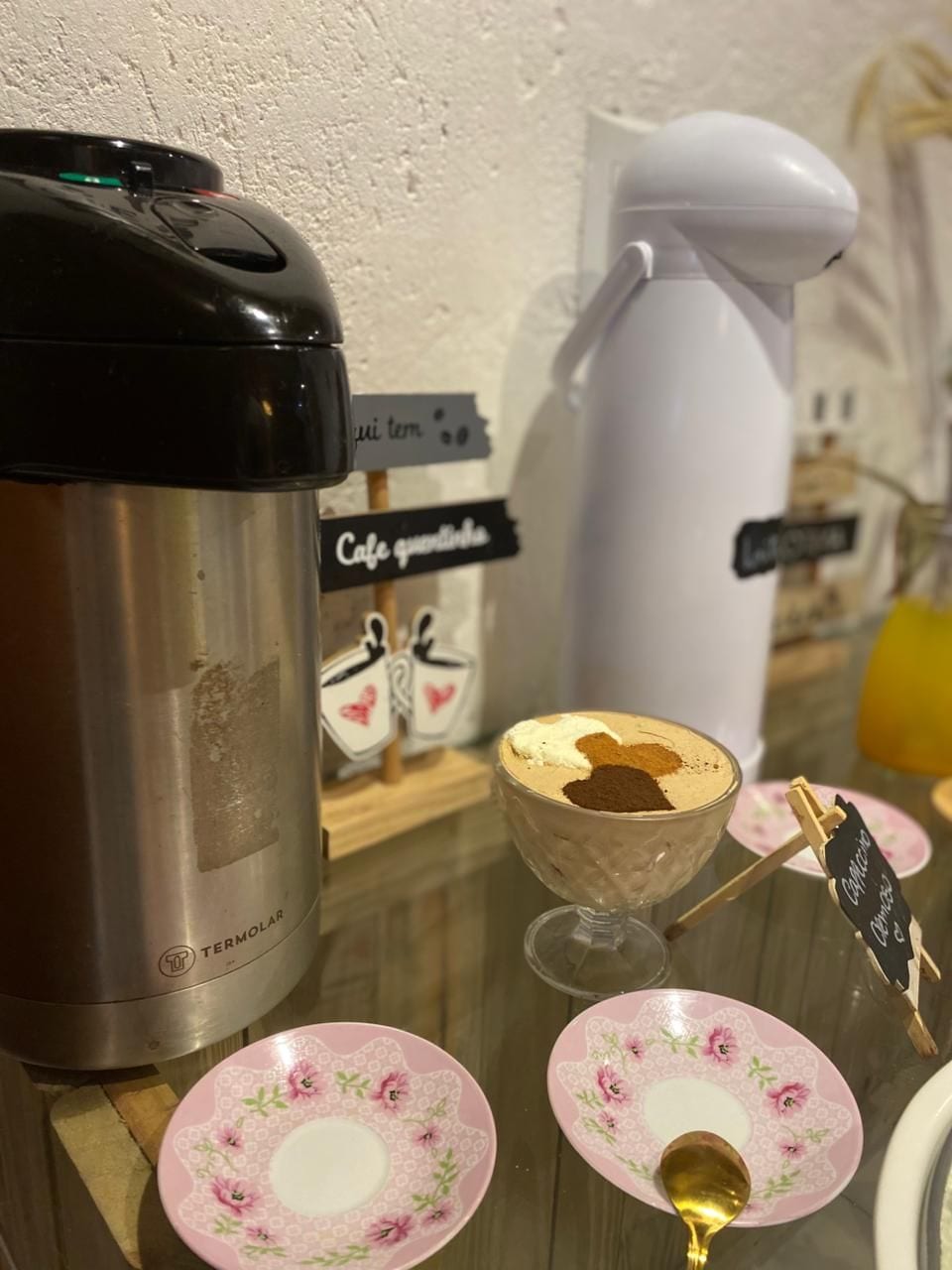 En kaffemaskine, en termokande, et skilt med 'Cafe' og en kop kaffe på et bord.