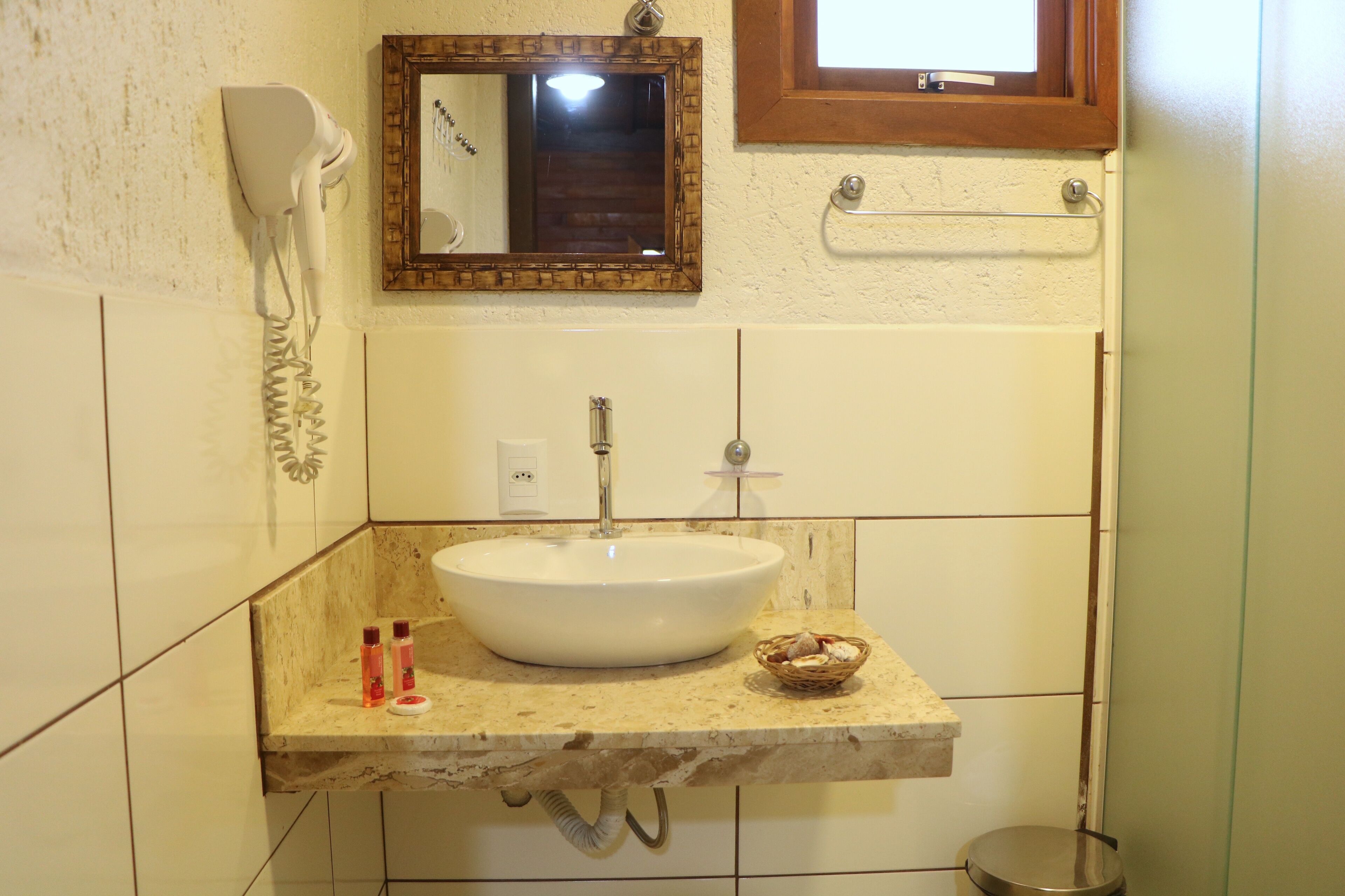 A bathroom with a white sink, a hairdryer, a mirror, and a window.