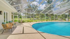 A covered outdoor swimming pool with a clear view of a green landscape and a white building in the background. - Cozy Ocala Retreat w/ Pool, Screened Lanai! (Ocala)