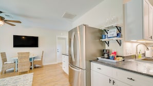 A modern kitchen with a stainless steel refrigerator, white cabinets, and a dining area with wicker chairs. - Cozy Ocala Retreat w/ Pool, Screened Lanai! (Ocala)