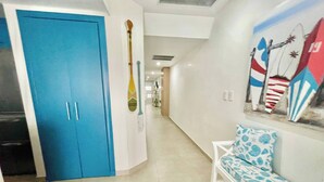 Un pasillo con una puerta azul, un banco blanco y un mural con pinturas de tablas de surf.