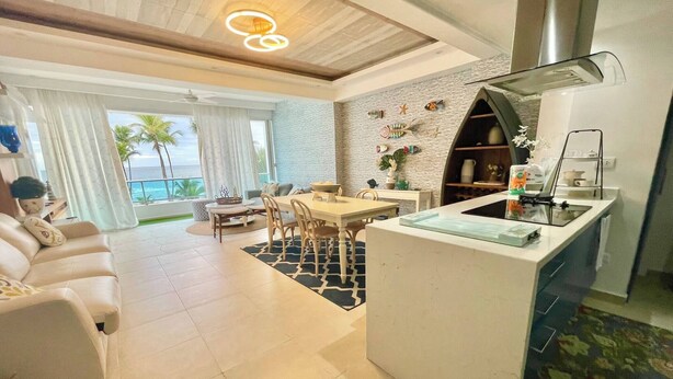 Una sala de estar moderna con comedor, una cocina con isla integrada y un amplio ventanal con vistas al océano.