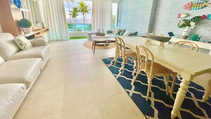 Una sala de estar moderna con comedor, un ventanal con vista a palmeras y una pared decorativa con objetos pequeños.