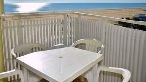 A balcony with a table and chairs, overlooking a beach and ocean.