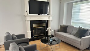 En moderne stue med pejs, fladskærms-tv, en grå sofa og et sofabord.